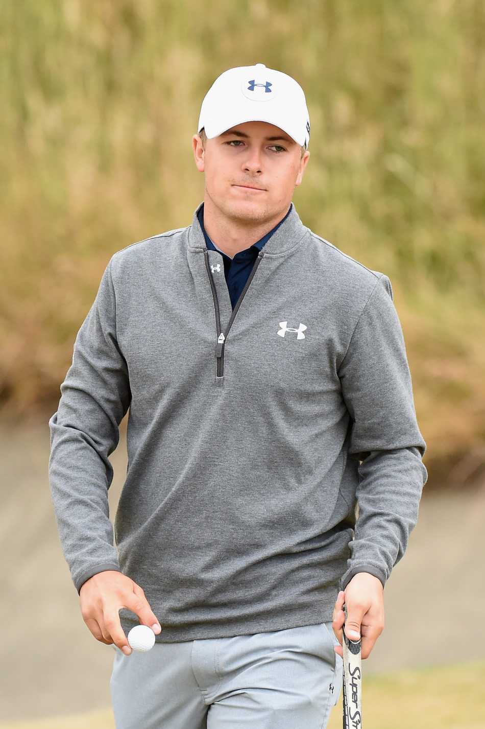 乔丹·斯皮思身着深蓝色上衣与浅灰色长裤，于绿茵球场上沉稳挥杆，经典灰调搭配尽显简约高级的时尚质感。