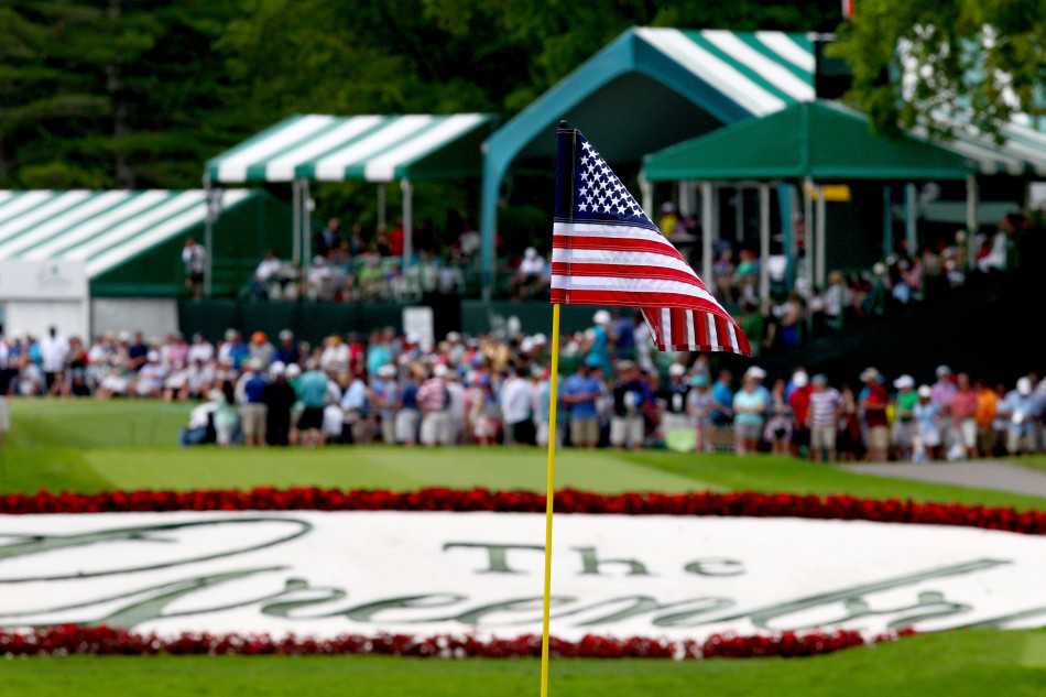 TPC老白球场第18洞，星条旗在高耸的旗杆上迎风飘扬，与翠绿的果岭和远处看台形成鲜明对比，独立日的阳光洒满整个球场。