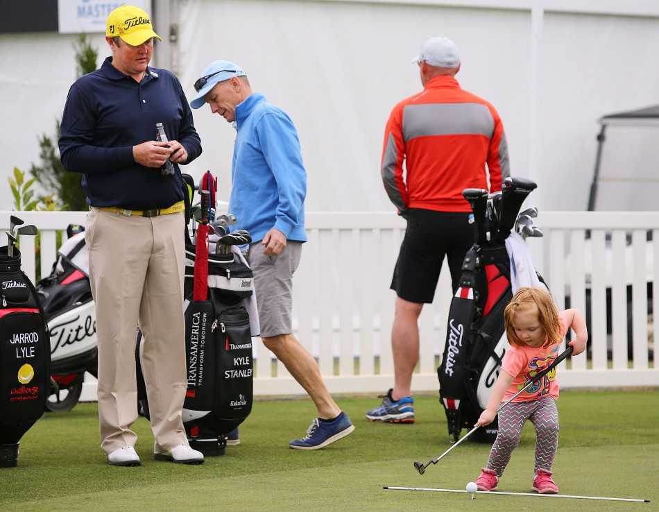 金发小女孩踮着脚尖专注观察父亲手握推杆的姿势，阳光在她睫毛上跳跃