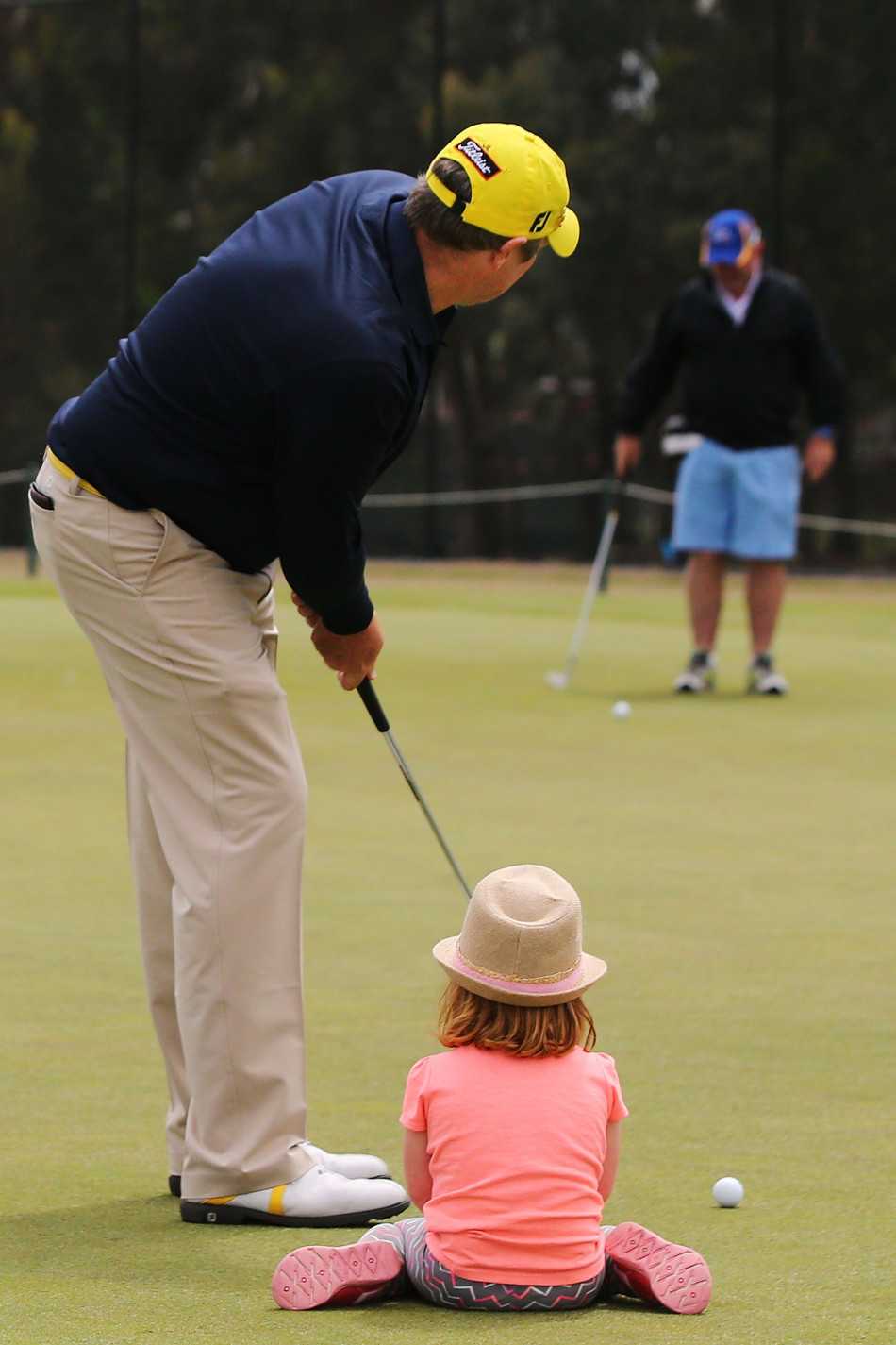 父亲手把手教导女儿推杆技巧，两人的影子在草地上交叠成温馨的画面
