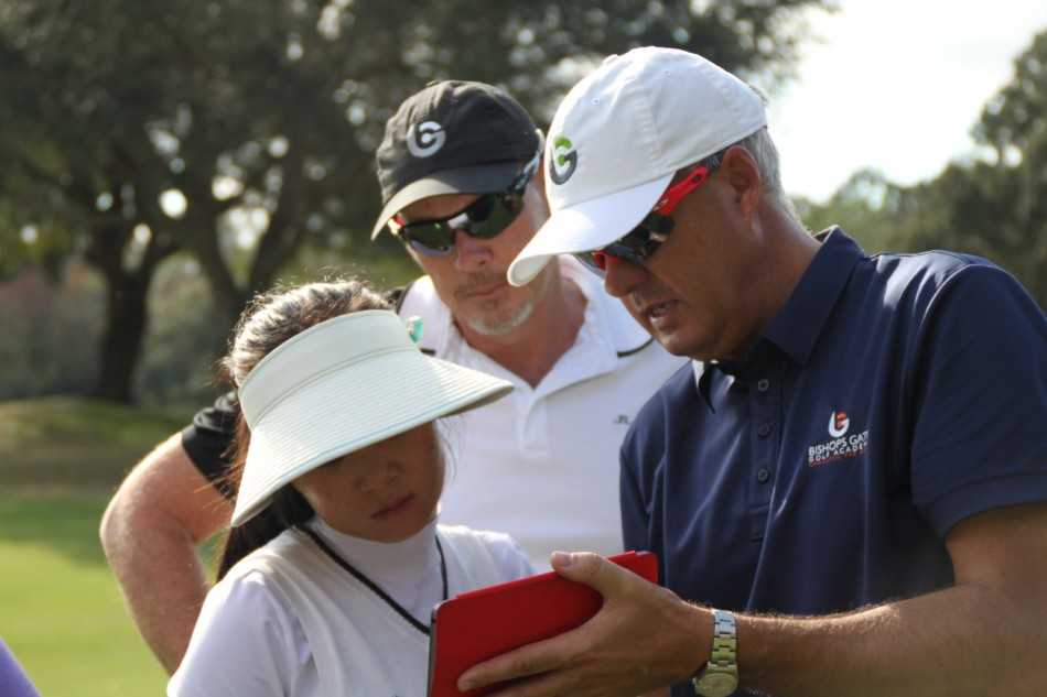 教练手持数据分析板，与学员热烈讨论着挥杆动力学的原理，背后的屏幕上展示着理想与实际挥杆路径的对比图