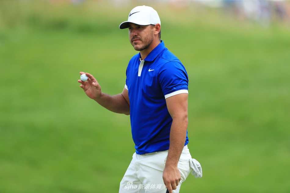 球场全景，绿意盎然的球道与湛蓝的水障碍构成和谐画面，一名球童正在远处为球员服务