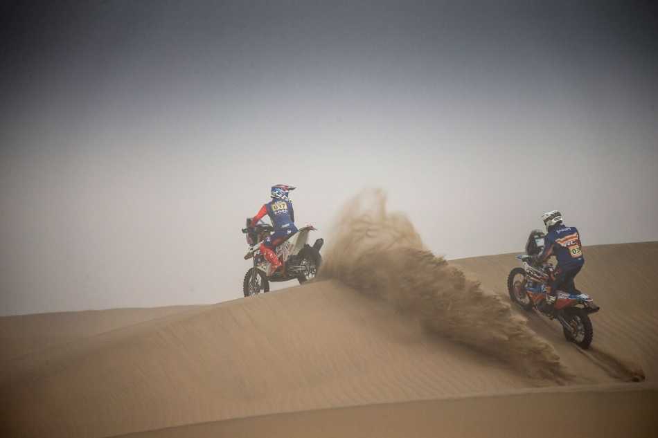 摩托车手在终点线前全力冲刺，紧绷的身体与专注的目光凝聚着穿越漫漫黄沙后对胜利的最后冲刺。