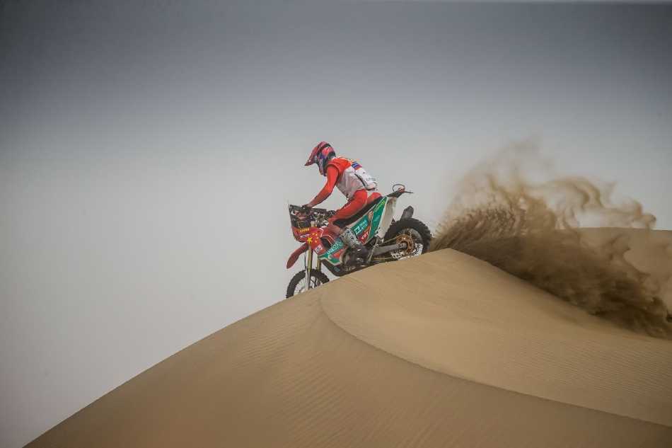 赛车从高大沙梁顶端疾驰而下，车头下探，仿佛投入金色海洋的怀抱，激起汹涌沙浪，气势磅礴。