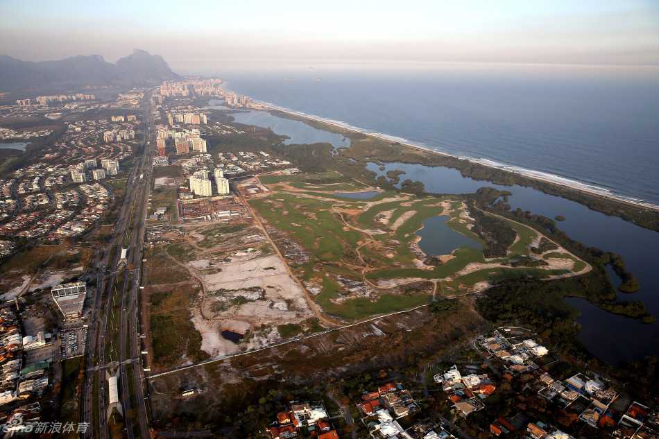 俯瞰视角下，球场蜿蜒的球道与碧蓝的水障碍交织，如同在大地铺开的翡翠色绸带，与远处城市的轮廓遥相辉映