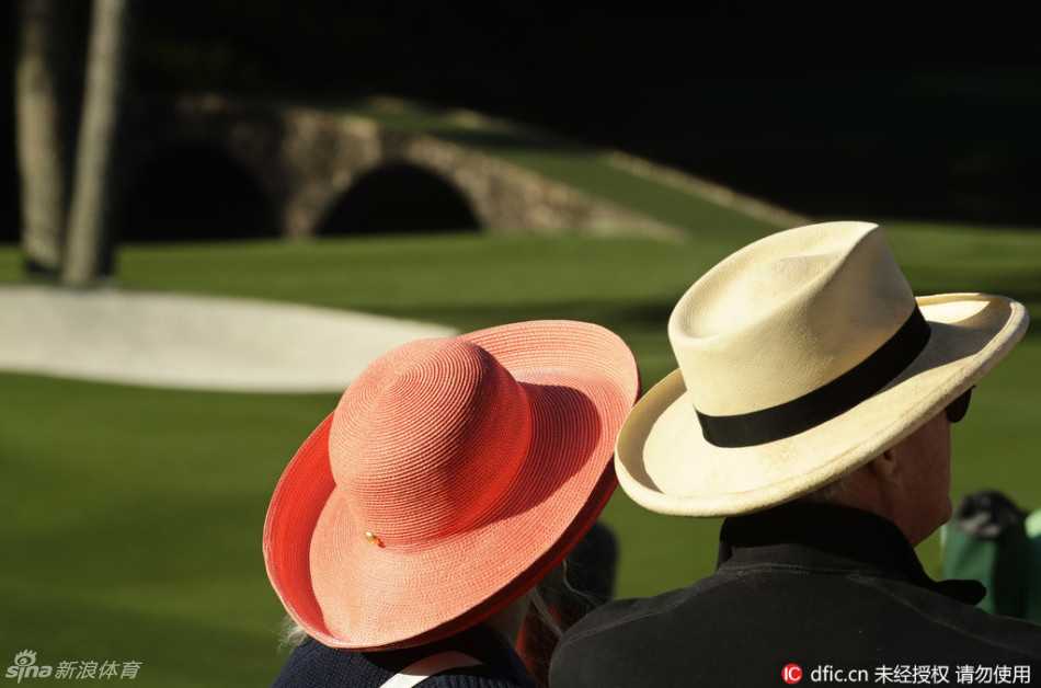 在果岭边缘的休息区，一位小男孩正全神贯注地盯着手机屏幕，而他身旁的成人则手持望远镜，认真观察着球员的每一次击球。