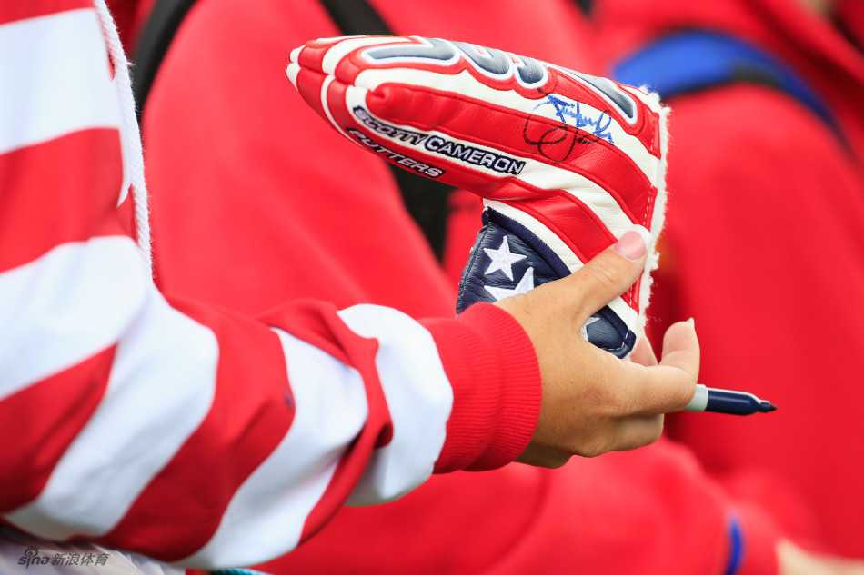 一位狂热的高尔夫球迷头戴插满各色莱德杯纪念徽章的帽子，如同一位凯旋的将军展示战利品。