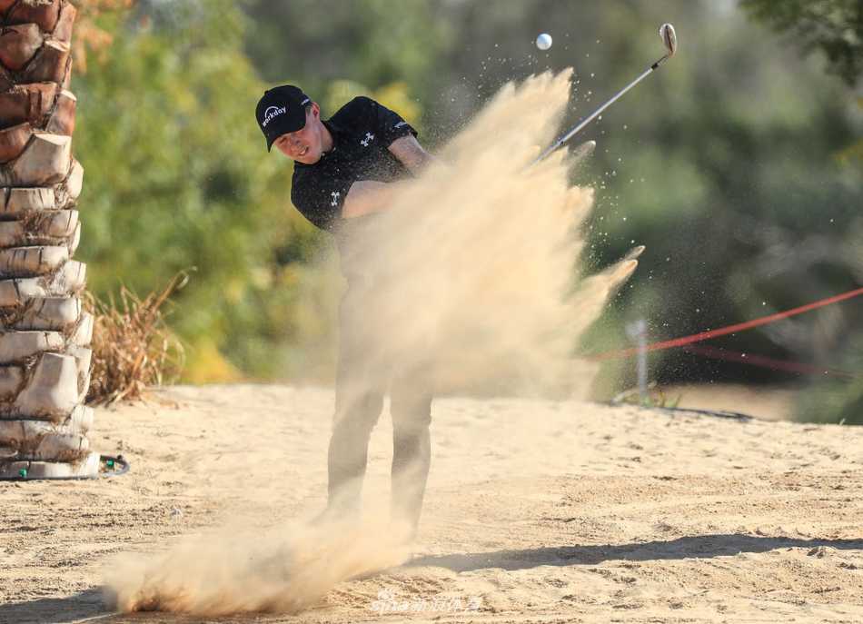 中国小将林钰鑫在沙坑中救球，身体姿态舒展有力，沙尘扬起，画面充满动感