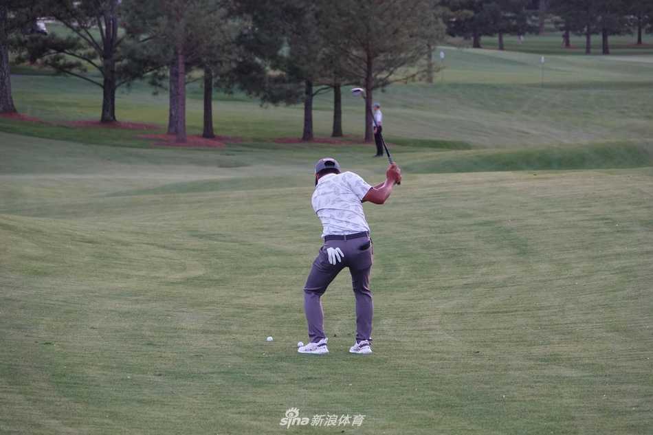 潘政琮俯身轻轻拾起一颗高尔夫球，背后是奥古斯塔标志性的会所与盛开的杜鹃花丛。