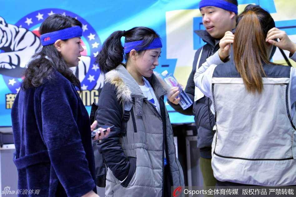 一位背着专业器材包的记者侧身而立，头上的发带格外清晰，背景是模糊的球场灯光和人影，这张照片定格了CBA历史上媒体以独特方式参与其中的经典瞬间。