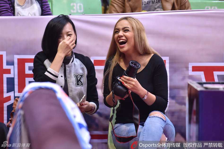 篮球传奇姚明与奥尼尔并肩坐在场边，姚明目光专注地凝视着赛场方向，眼神中既有对老友的亲切，也有对眼前比赛的深思，仿佛瞬间回到了当年两人并肩作战的岁月。