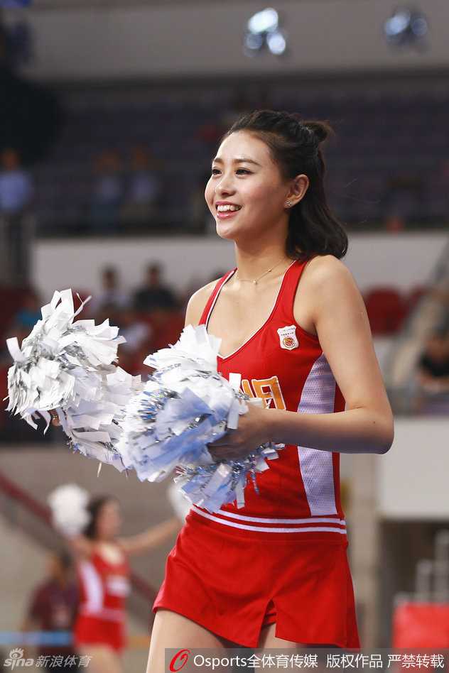 一位笑容极具感染力的篮球宝贝在赛场边回眸，飘逸的长发和靓丽的外形让她成为了相机追逐的焦点，背景是模糊的观众席，更显她的光彩夺目。