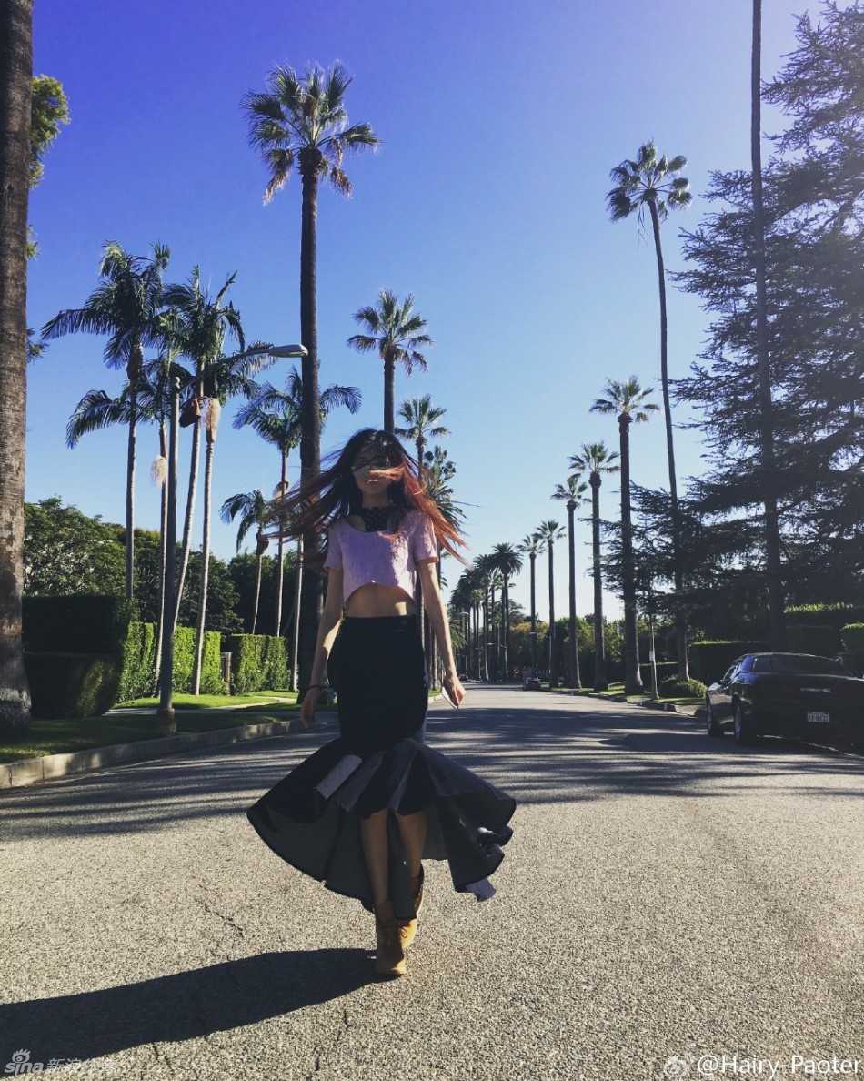 李跑身着休闲装扮，在异国建筑的背景下回眸一笑，一双美腿在阳光下显得格外修长，画面充满时尚街拍的随意感。