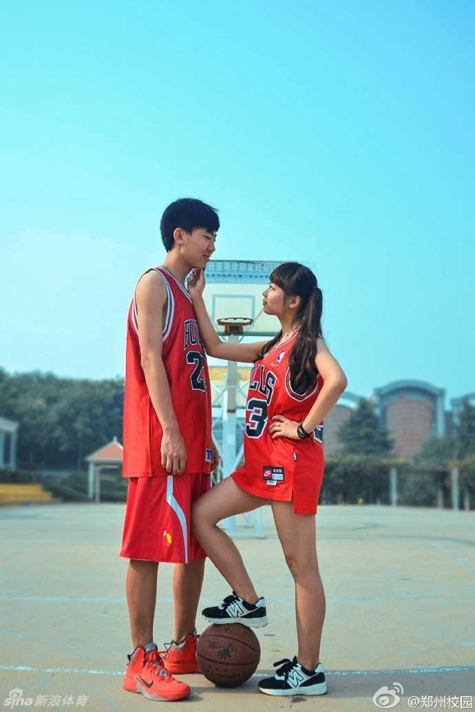 运动过后，穿着球衣的少年和女孩在篮球架下休息，少年调皮地对着镜头敬礼，女孩则在一旁温柔地看着他，背景是绿色的球场围栏，画面充满了青春活力。