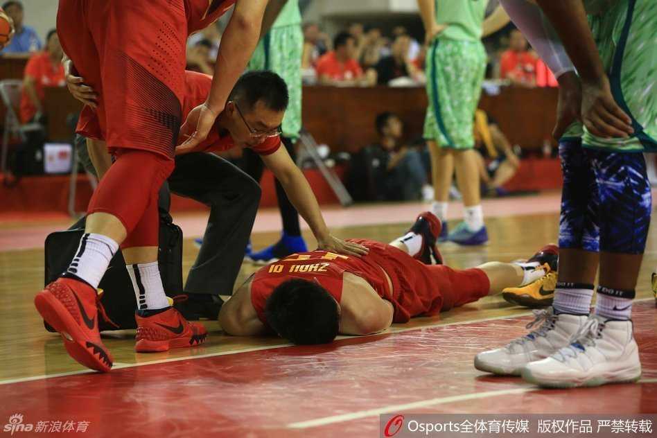 回到场边的周琦坐在板凳席上，队医仍在为他进行细致的检查和处理。周琦低头看着自己的伤处，神情落寞，身旁的队友们也神色凝重，默默关注着他的情况。