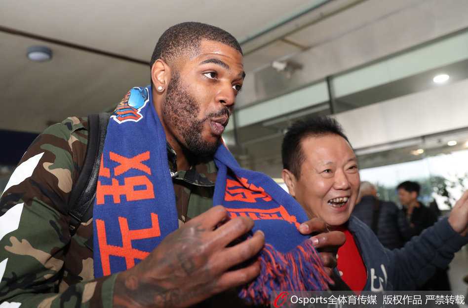 在酒店房间里，约什坐在床边，身边摆放着几个行李箱，他正低头专注地滑动着新手机的屏幕，似乎在学习刚装上的微信和微博。