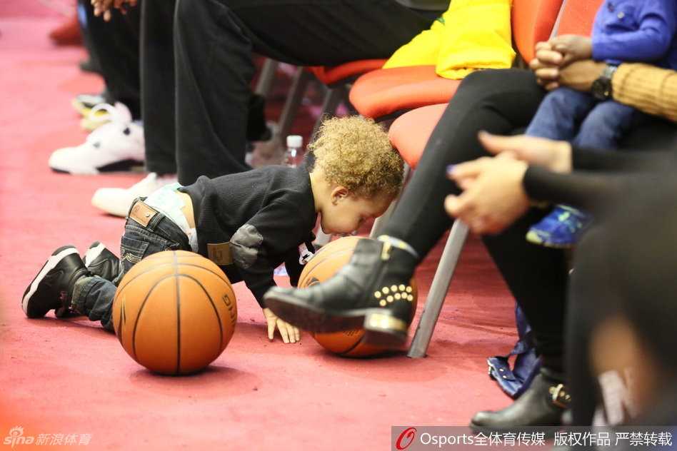 小儿子张开双臂与哥哥争宠，踮起脚尖想要亲吻哥哥手中的篮球，兄弟俩的可爱互动让身后的妈妈也忍俊不禁