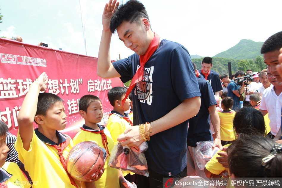 李晓旭面带微笑，单膝点地俯身为身前的小球迷在篮球上签名，周围的小朋友用崇拜的眼神紧紧盯着他的一举一动。