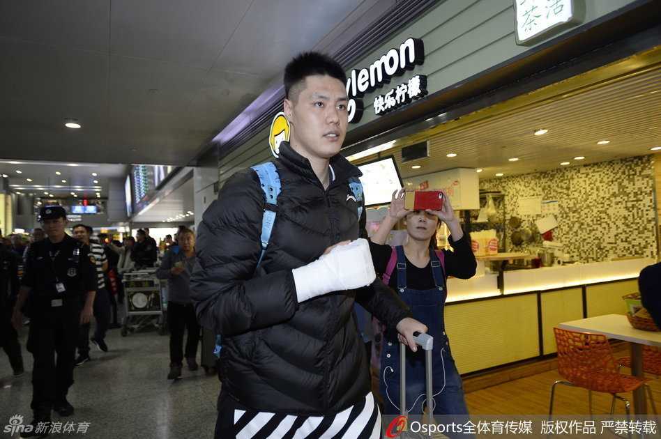 身穿红色外套的刘志轩低头快步行走，身旁的安保人员警觉地观察着四周，身后的球迷们举着手机，试图记录下这历史性的一刻。