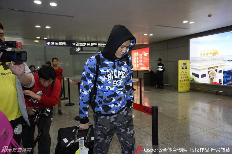 一名戴着眼镜的辽宁女球迷，脸颊上同样贴着一块蓝色创可贴，她双手举着手机，眼神热切地望向正在走来的球员，脸上满是兴奋与期待。