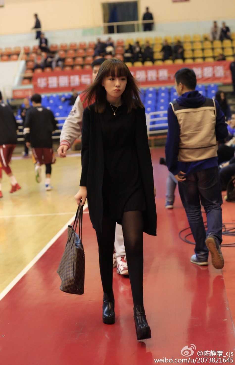 一位身材高挑的女球迷身穿便装，快步穿过体育馆的通道，脸上带着急切而期待的神情，准备进场观看八一男篮的比赛。