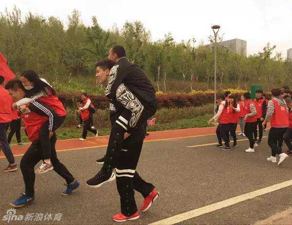 西热力江背着队友阿不都沙拉木奋力前行，两人脸上洋溢着笑容，在公益跑的游戏中默契配合，展现了深厚的兄弟情谊。