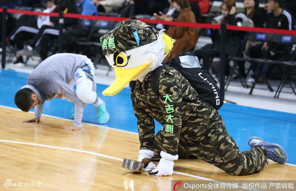 霹雳鸭身穿特制的宽大球衣，在通道入口处即兴模仿起了球员的赛前热身动作，有模有样地压腿拉伸，夸张的动作幅度让路过的裁判员都忍俊不禁。