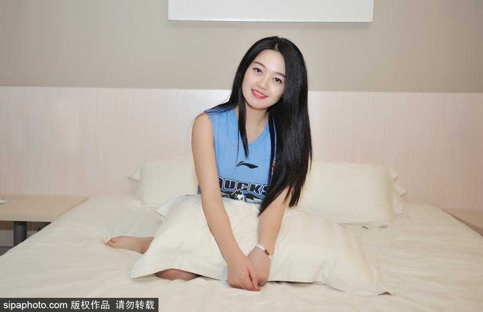 画面中的女孩安静地坐在床边，手托下巴，眼神温柔却坚定。她身穿的休闲服上，一枚小小的首钢队徽在灯光下闪闪发亮，细节之处尽显铁粉本色。