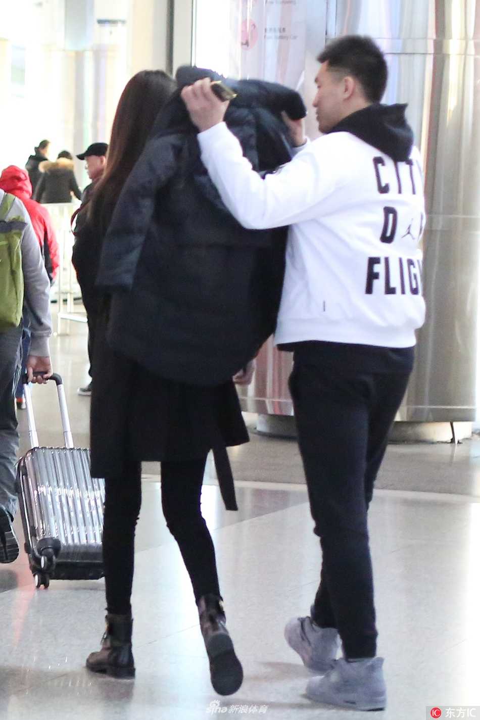 郭艾伦身着休闲装，安静守候在机场到达大厅，手中紧握着一杯刚买好的热咖啡，目光穿过人群，专注地寻找着熟悉的身影，脸上洋溢着期待的微笑。