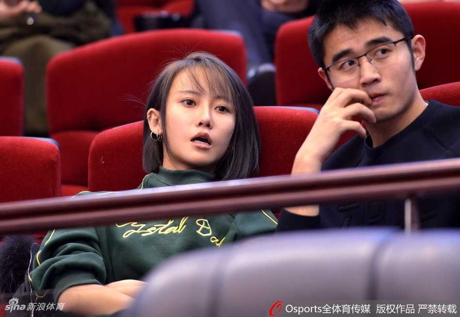 一位气质优雅的女球迷，手持加油棒，目光坚定地望向球场中央，在激烈的比赛氛围中显得格外从容和投入。