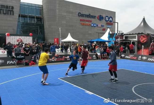 一群少年在球迷专区的迷你篮球场上腾空跃起，橘色皮球在空中划过弧线，背景是巨大的欧冠联赛标志，青春的活力和梦想在此刻定格。