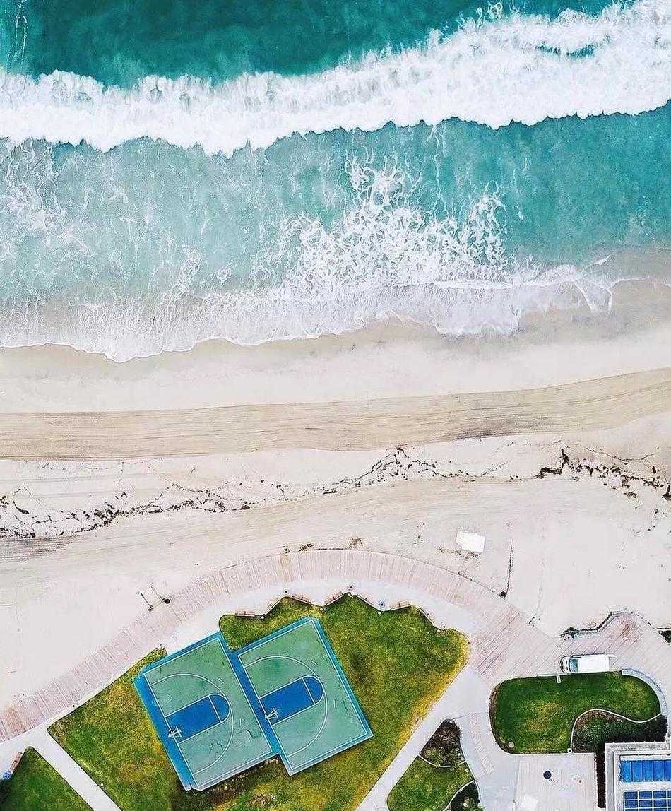 夕阳西下，阳光斜射进室内篮球馆，高大的落地窗、光洁的木地板和远处的篮筐构成一幅宁静深邃的纵深感画面。