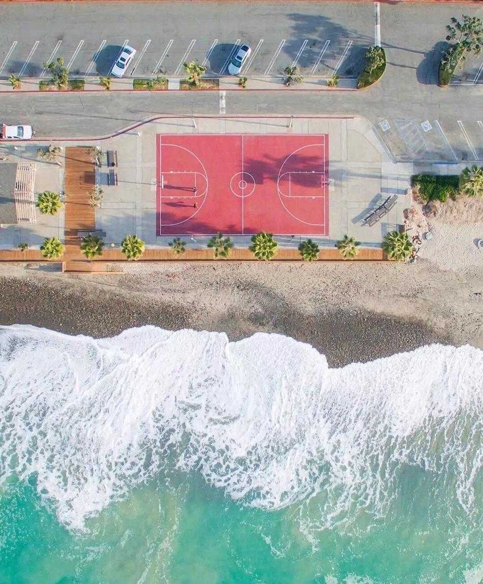 正午阳光直射，篮球场地板上出现清晰的几何阴影区，空无一人的球场在强烈光线分割下，展现出极简主义的冷静美感。