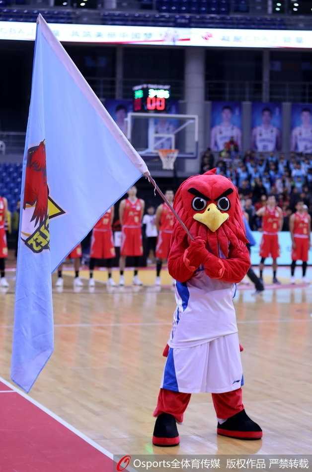 青岛啦啦队宝贝在场边稍作休息，她低头查看手机，金色的亮片上衣在灯光下闪烁，与场上紧张激烈的比赛形成有趣对比，展现了赛场花旦在动与静之间的瞬间转换。