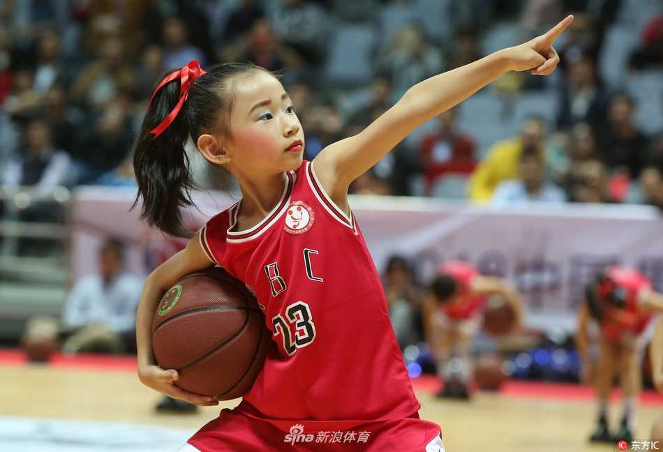 一个小球员紧紧抱着比自己小不了多少的篮球，安静地站在场边，望着远处正在热身的职业球员，眼神里充满了憧憬与向往。