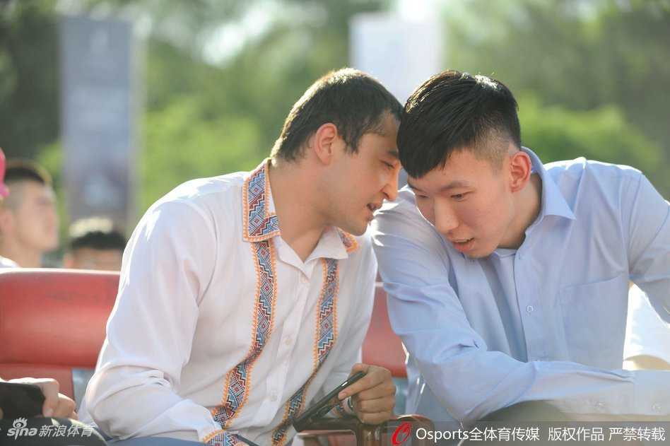 李根与周琦面对面站立交流，身后的李秋平指导双手背后，目光越过人群静静注视着崭新的车辆，仿佛在沉思下赛季的卫冕之路。