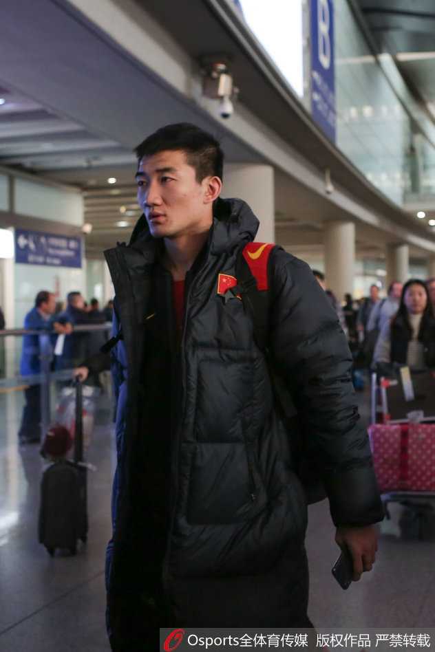 王哲林身穿红色国家队队服，尽管经历了漫长的赛季和激烈的世预赛，但他在行李传送带旁依然显得精神饱满，与队友说笑。