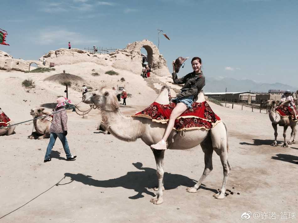 许诺展现出旅途中的悠闲一面，她侧身对着镜头，手里拿着一杯饮品，脸上带着轻松惬意的表情。简单的穿着打扮难掩其高挑身形，一双美腿在自然光下显得格外白皙瞩目。