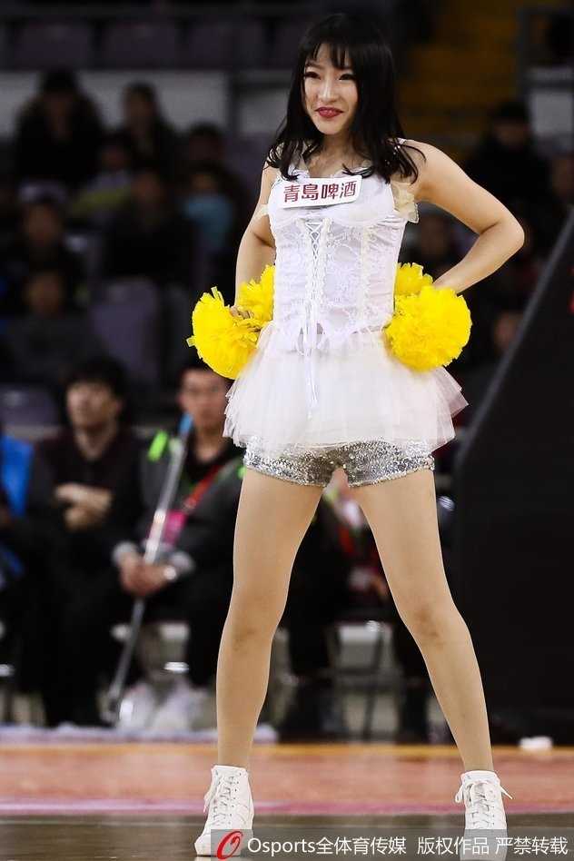 镜头聚焦于一位领舞的篮球宝贝，她扎着清爽的马尾辫，在聚光灯下展现着自信而妩媚的笑容，手中的花球随着动感的节奏在空中划出优美的弧线。