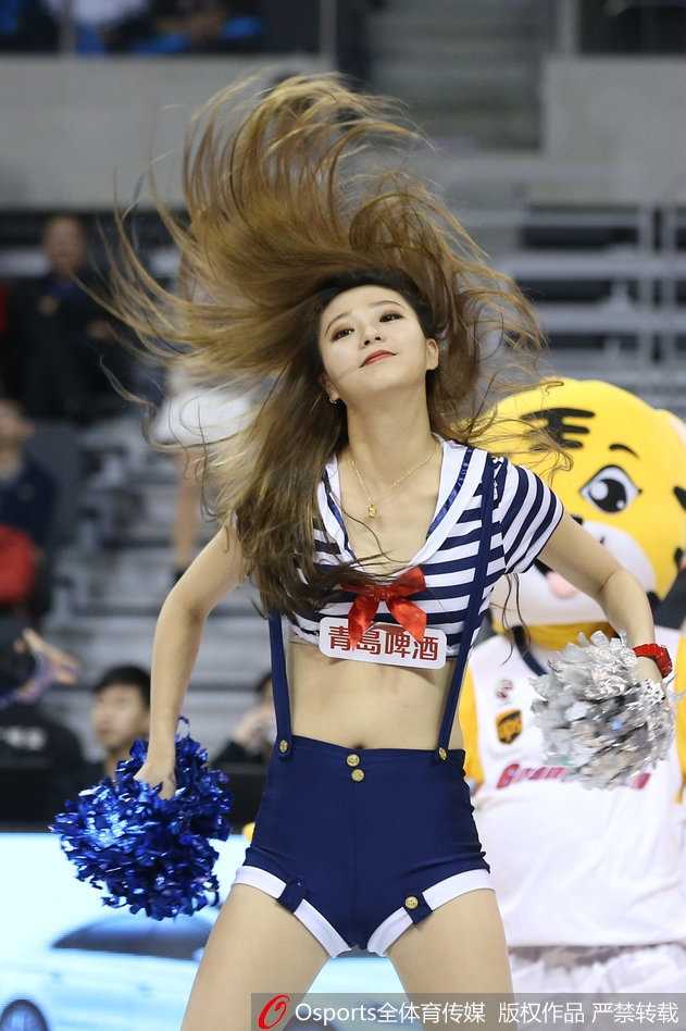 侧面特写捕捉到一名长发宝贝旋转的瞬间，虎尾造型的腰饰随着身姿摆动，脸上洋溢着自信的微笑，背景是虚化的球迷看台，整个画面充满动感与张力