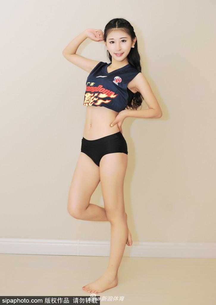 一位篮球宝贝坐在场边的篮球上，双手撑着膝盖，对着镜头露出灿烂的笑容，汗水仿佛还挂在额头，洋溢着青春的朝气。