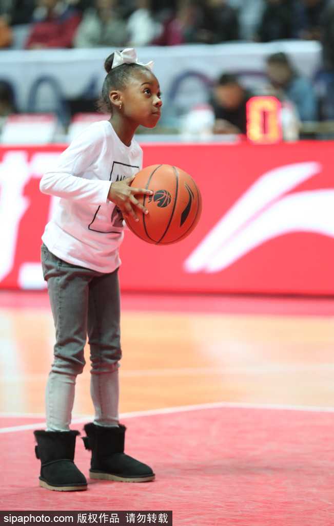 哈德森的小女儿穿着可爱的粉色棉服，双手紧紧抱着比她小不了多少的篮球，眼神专注地盯着场上的父亲。