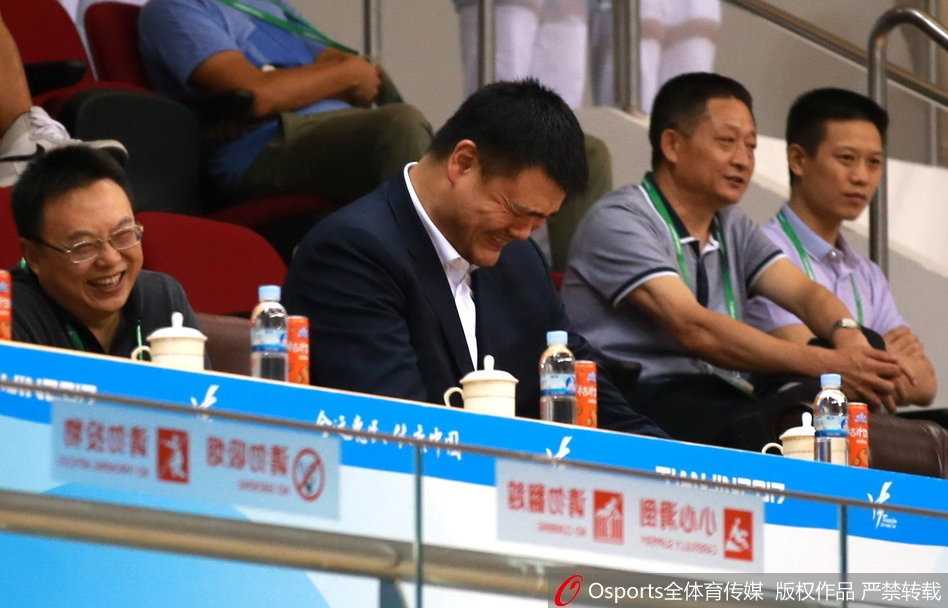 在周围喧嚣的环境下，姚明双手托腮，目光如炬地凝视着球场中央，仿佛一位正在构思宏伟篇章的雕塑家，将所有的思绪都藏在了那宽厚的掌心之后。