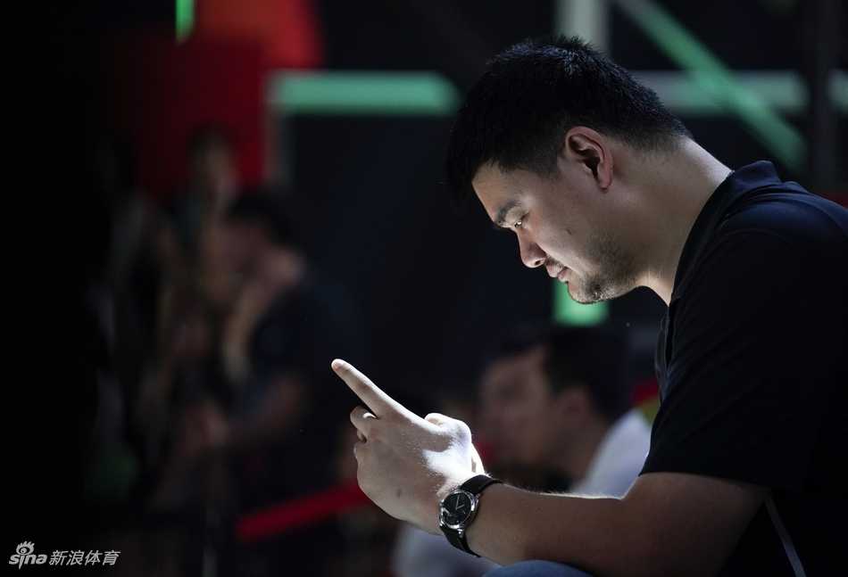 姚明在台下落座，神情专注地看着场上的表演或比赛，嘴角带着一丝欣慰的笑意，身边的嘉宾也正聚精会神，共同欣赏这场属于草根篮球的盛宴。