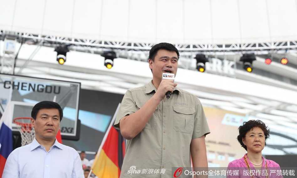 姚明坐在看台上专注地观看揭幕战，他双手搭在膝盖上，神情严肃而投入，仿佛比场上的球员更加紧张。