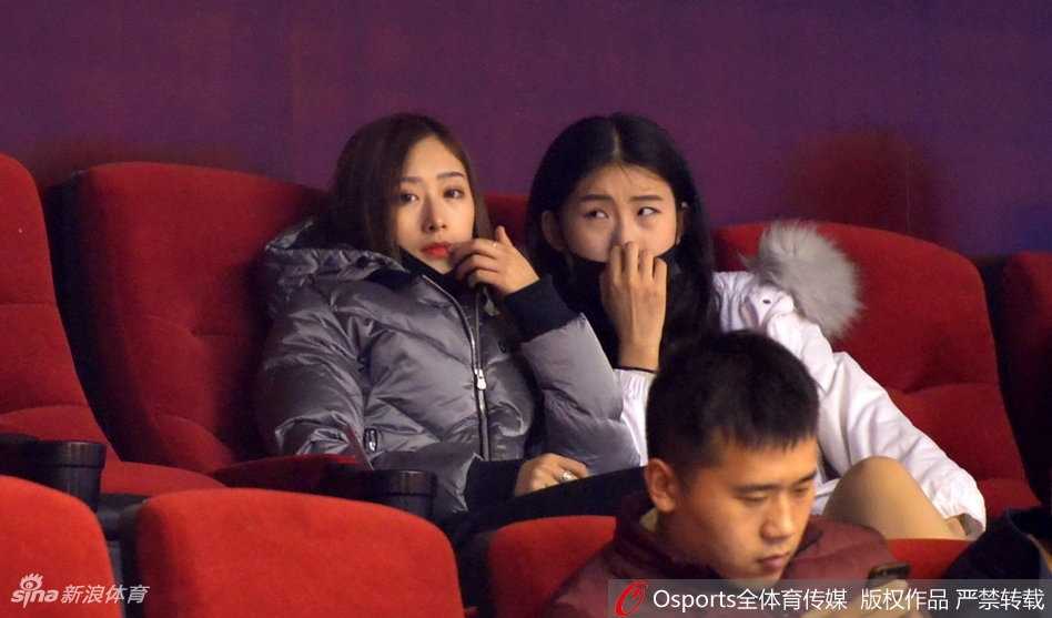 丁彦雨航女友戴着时尚口罩，眉眼含笑与身旁的睢冉妻子窃窃私语，两人在球迷看台上显得格外引人注目。