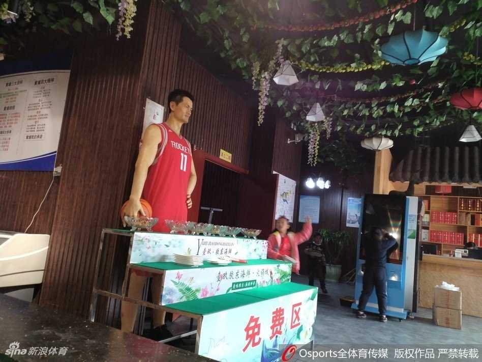 蜡像独自伫立在装饰着中国红灯笼的饭店大厅里，中西元素在此奇妙融合，它像是一个沉默的守护者，静静注视着往来的食客