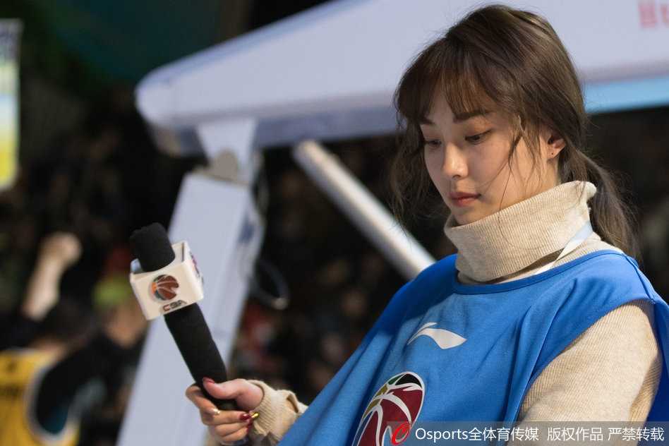 在明亮的场馆灯光下，美女主持侧身回眸，嘴角带着浅浅笑意，那份从容与优雅与身后座无虚席的看台相映成趣。