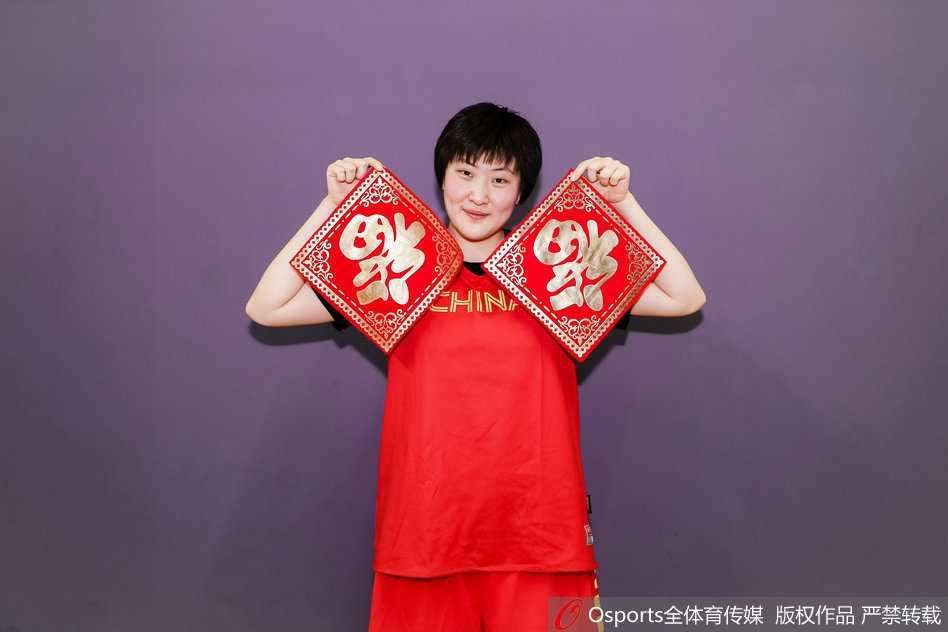 全体队员与教练组的大合影，大家簇拥在一起，有的竖起大拇指，有的挥舞着国旗，画面中充满了积极向上的能量，完美诠释了中国女篮团结拼搏的精神风貌。