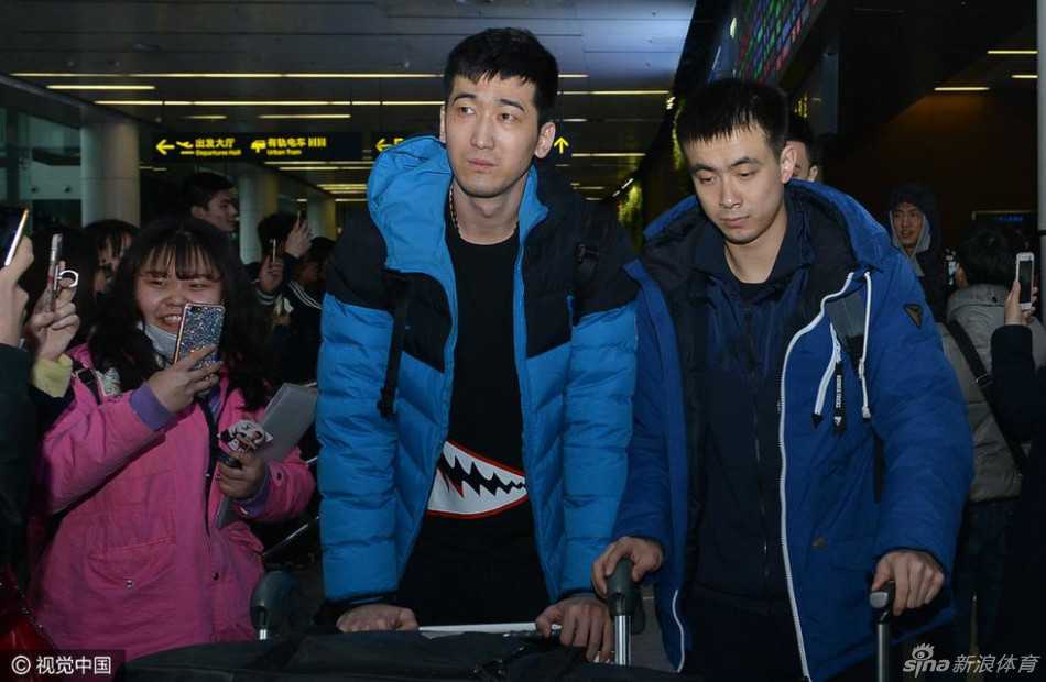 刘志轩身穿深色休闲服，神情虽显旅途劳顿后的倦意，但嘴角上扬露出温和的笑容，正与一位男球迷并肩站立合影，眼神中透着谦和。